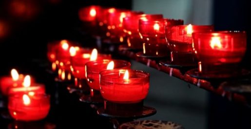 Several Small Diagonal Rows Of Red Candle Glasses All Alight In Darkened Room.