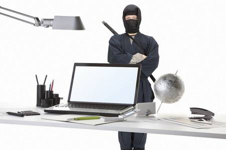 Computer Ninja Standing Behind Desk Arrayed With Several Tools/Tech Devices.