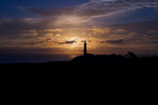 Featured Image Of An Unlit Shadowed Lighthouse At Sunset.