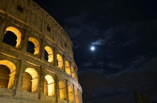 Image Of Romes Colisseum On A Clouded Moonlit Night With Most Of Moon Covered.