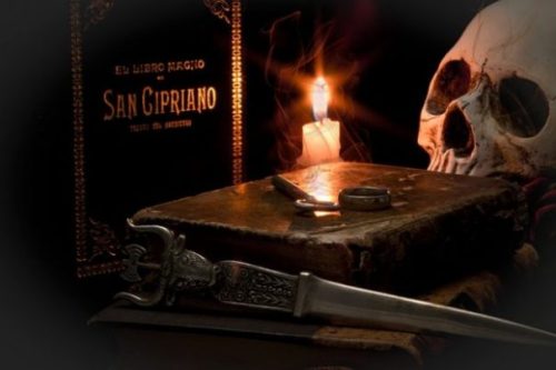 Featured Image Ancient Magic Ritual Scene. Grimoire, Skull, Candle, Ring, Key, Book and Knife Arranged Around Candle Lit Background. Ring And Key On Top Of Book.