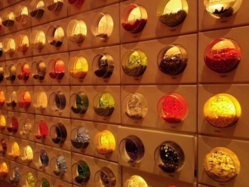 A Large Section Of A Wall Display With Rows Of Many Rounded Canisters Filled With Lego Pieces.