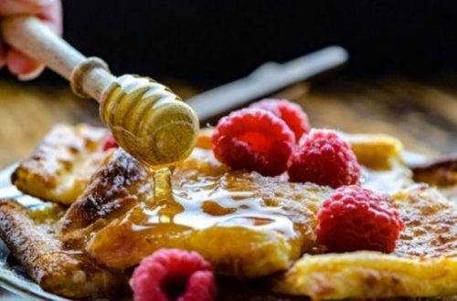 Featured Topic Image Of A Plate With A Pancake Raspberry Adorned Being Covered In Honey From A Wood Roller Implement.
