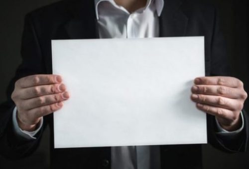 Man In Suit Holds Up A Piece Of Blank Paper.