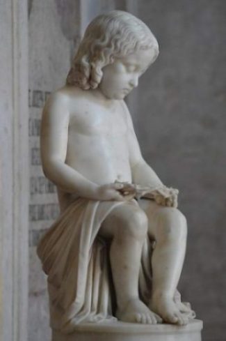 Featured Topic Image A Statue Of A Seated Child Looking At An Object In Their Hands.