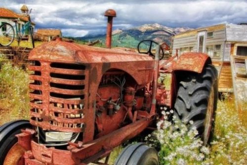 Image Of An Old Tractor In A Field Backgrounded By A Caravan And Cottage.