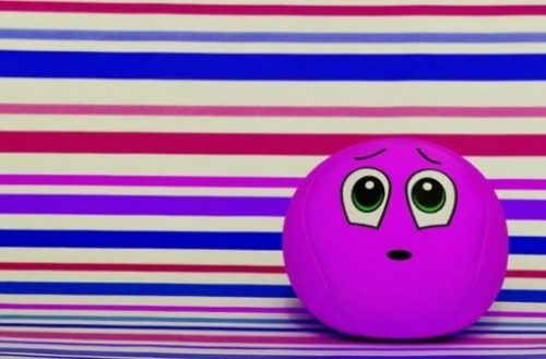 Featured Image Of A Purple Faced Ball Toy In Front Of A Striped Background.
