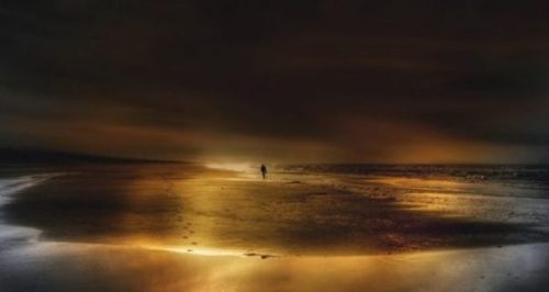 Image Of Beach Sunset With A Distant Figure And Footprints In The Sands.