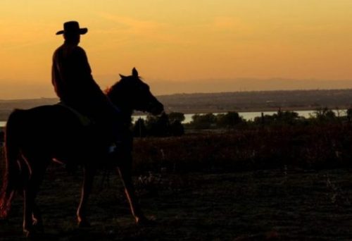Image Of A Cowboy On A Horse Overlooking A Sunset Lit Town.