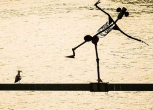 Featured Image Of A Metal Man Statue Leaning Over Water Whilst A Seagull Looks On.