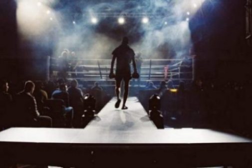 Image Of A Boxer Approaching The Lit Ring With A Crowd Shadowed In The Background.