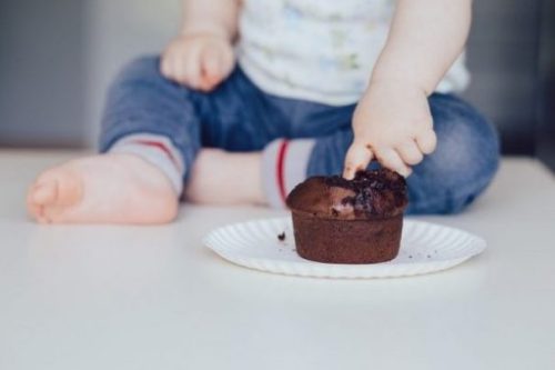 Featured Image Of A Floor Sitting Child Poking A Finger Into A Lone Large Chocolate Muffin.