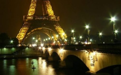Image Of Paris At Night Highlighting Lower Section Of Eiffel Tower And Bridge.